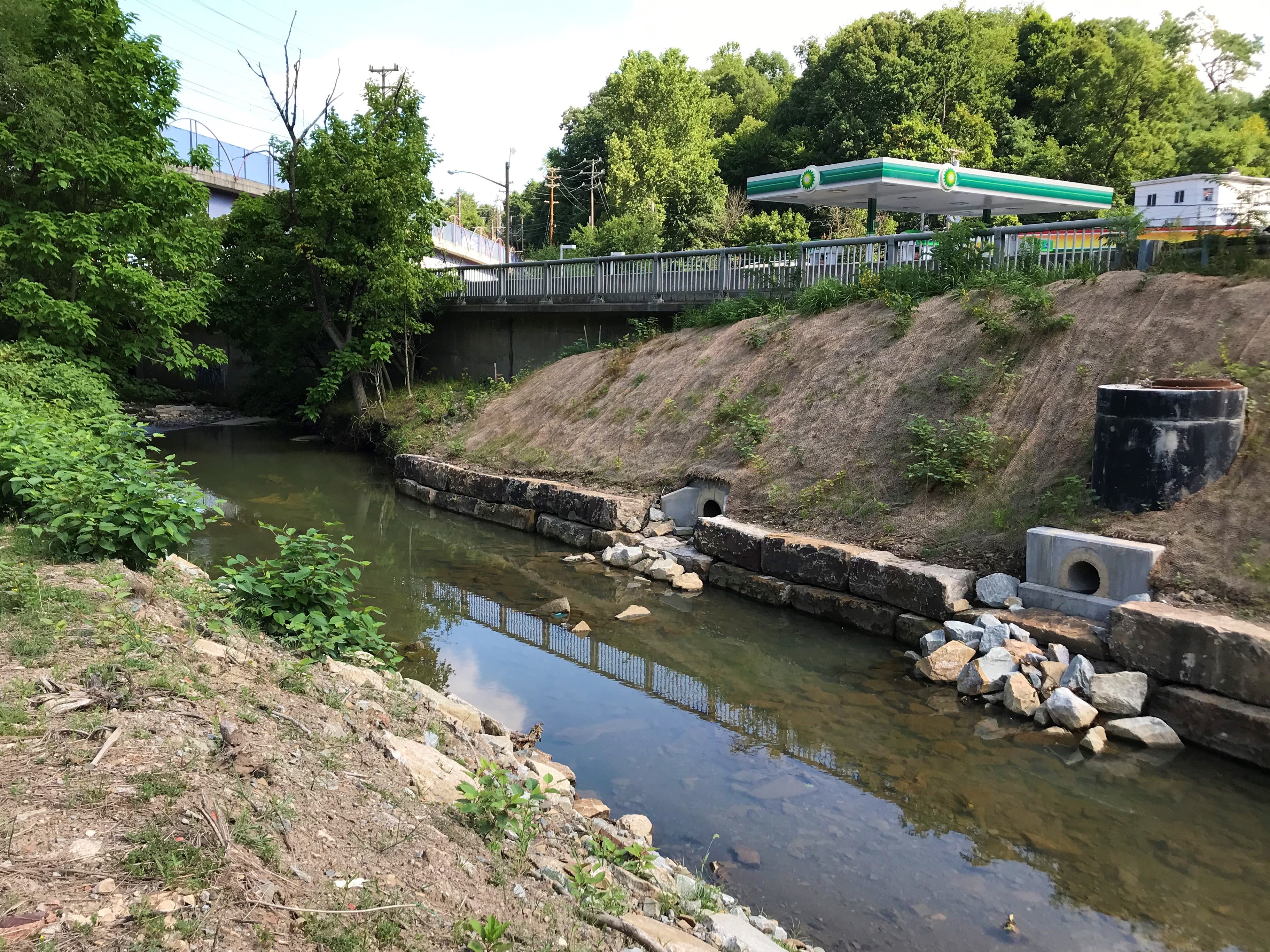 Photo of the Saw Mill Run stream restoration project by Ansonia Place, showing two restored storm sewer outfalls and boulders lining the stream