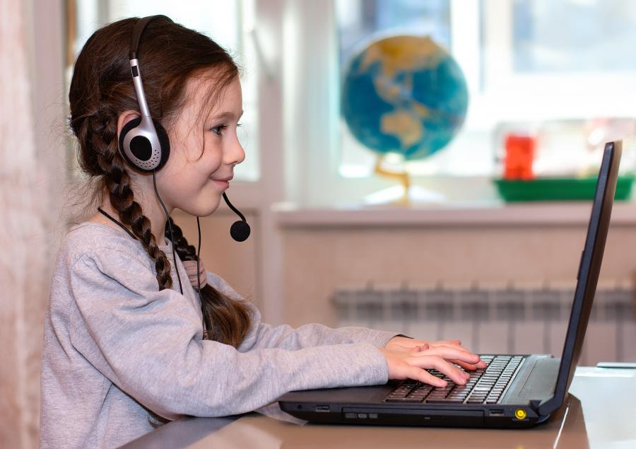 A girl with a headset on types on a laptop