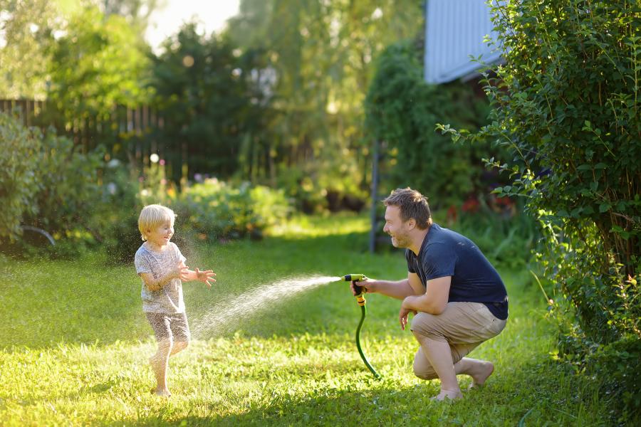 A father using an outdoor hose to cool off his son